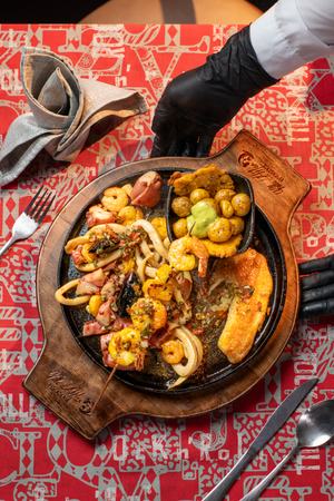 Delicious Colombian seafood platter with shrimp, squid, potatoes, and peppers on a sizzling hot plate.